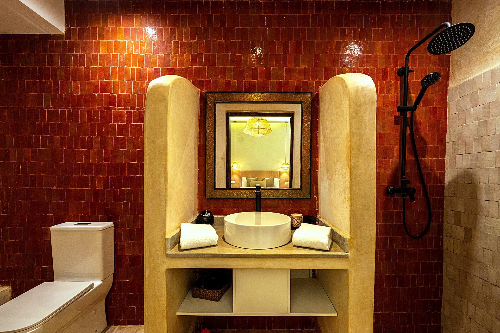 Un baño con pared de azulejos, un lavamanos con espejo, una ducha y un inodoro.