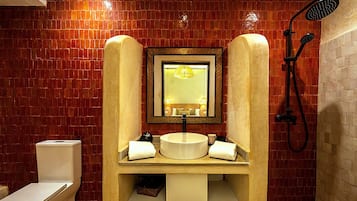 Ein Badezimmer mit gefliesten Wänden, einem Waschbecken mit Spiegel, einer Dusche und einem WC.