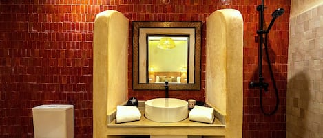Un baño con pared de azulejos, un lavamanos con espejo, una ducha y un inodoro.