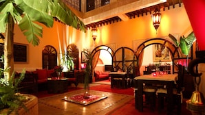 A cozy, well-lit indoor space with wooden furniture, a central fountain, and decorative arches. - Riad Jona (Marrakech)