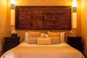 Un letto con una testiera decorata, numerosi cuscini e comodini con lampade.