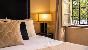 A neatly made bed with pillows, a bedside lamp, and a window with a decorative iron grille.