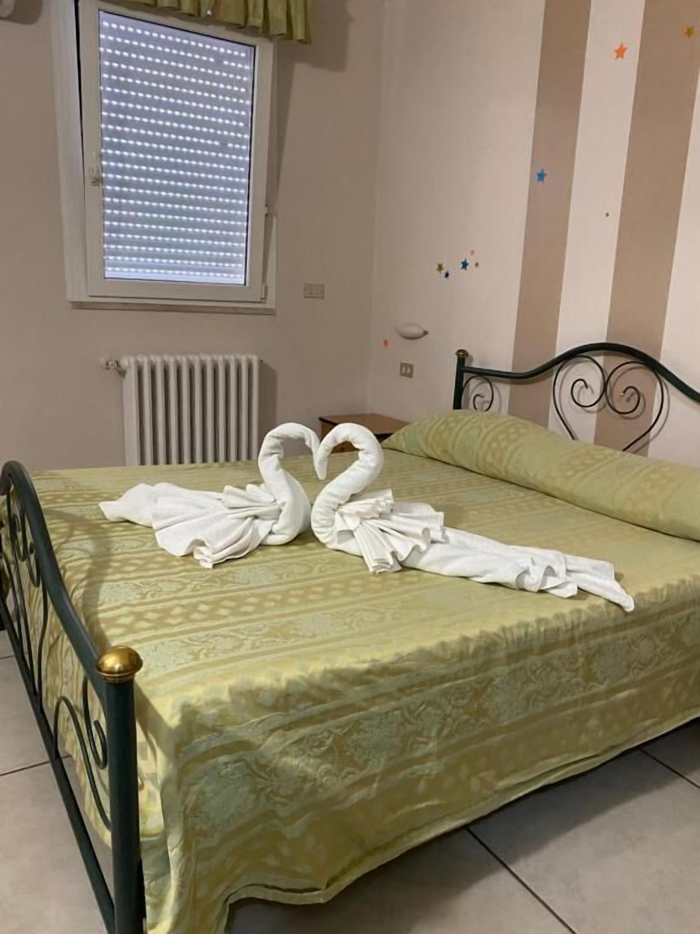A bed with a patterned bedspread, a radiator, and a window with blinds.