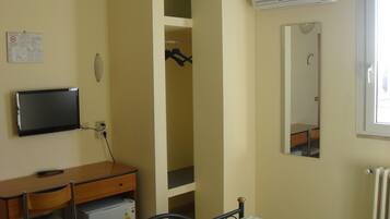 A bedroom with a bed, a desk with a computer, a wardrobe, and an air conditioning unit.