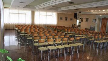 A large hall with rows of chairs, a polished floor, and large windows with curtains.
