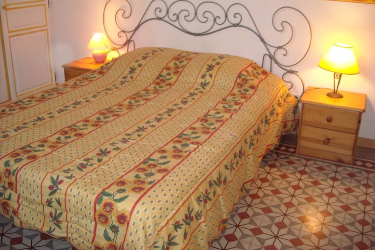 A bedroom with a floral-patterned bedspread, a metal headboard, two bedside tables with lamps, and a geometric-patterned floor.