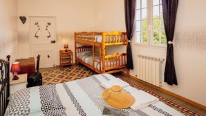 A bedroom with a bunk bed, a desk with a lamp, a suitcase, and a patterned bedspread. - Gîte des Figourières (Sainte-Anastasie)
