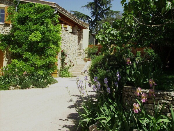 A stone building with a tiled roof, surrounded by lush greenery and flowering plants.