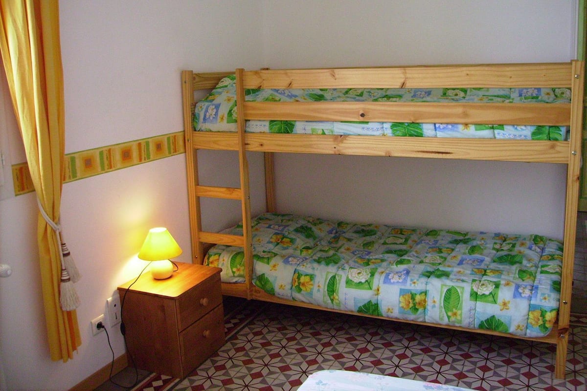 A bunk bed with floral bedding, a bedside table with a lamp, and a geometric patterned floor.
