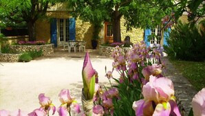 A garden with blooming flowers, a stone wall, and a building with blue shutters. - Gîte des Figourières (Sainte-Anastasie)