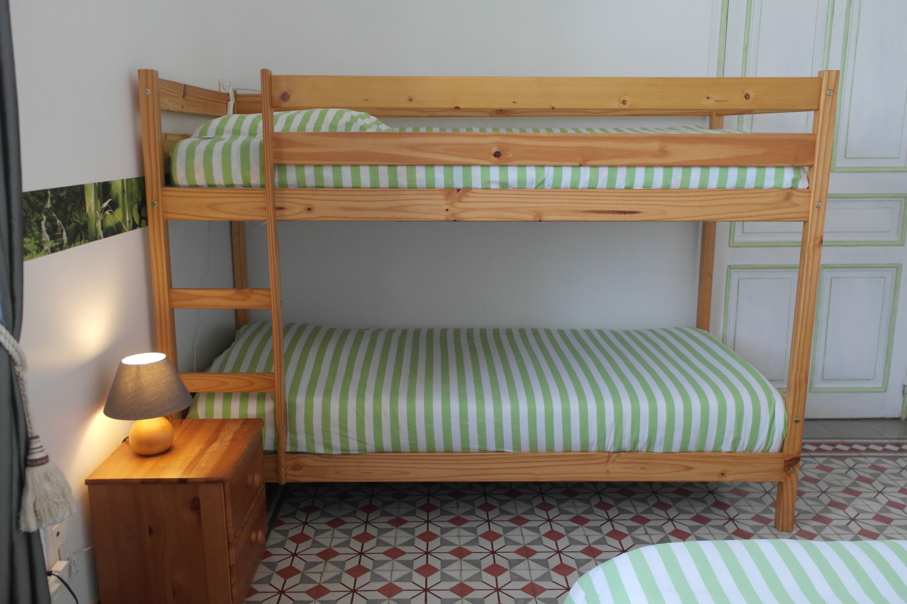 A bunk bed with green and white striped bedding, a wooden ladder, and a bedside lamp.