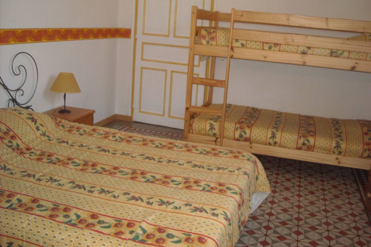 A room with a bunk bed, a small bedside table with a lamp, and a patterned bedspread.