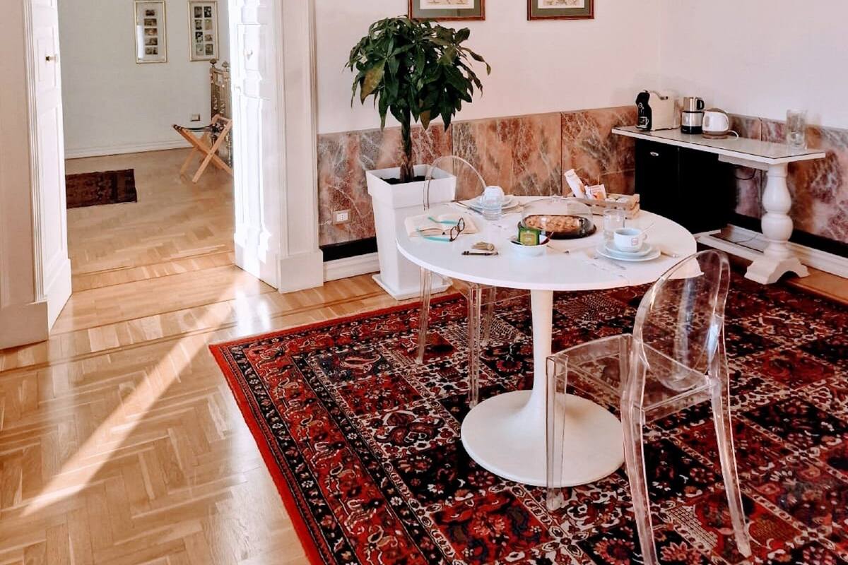 A dining area with a round table, chairs, a potted plant, and a patterned rug.