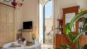 A room with a round table set for dining, a television on the wall, and a view of the outside balcony. - Palazzo De Giorgi (Lecce)