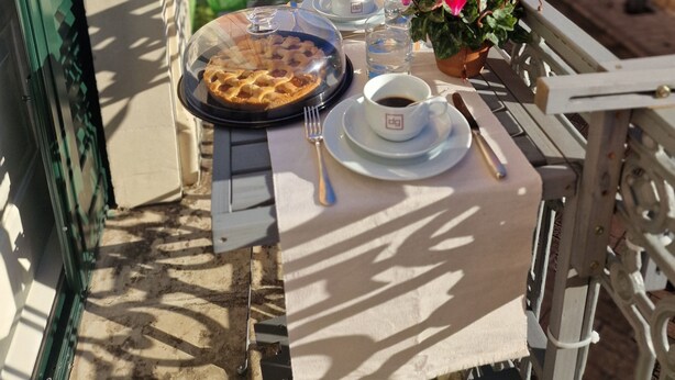 A balcony table set with a plate of food, a cup, and a glass of water. - Palazzo De Giorgi (Lecce)