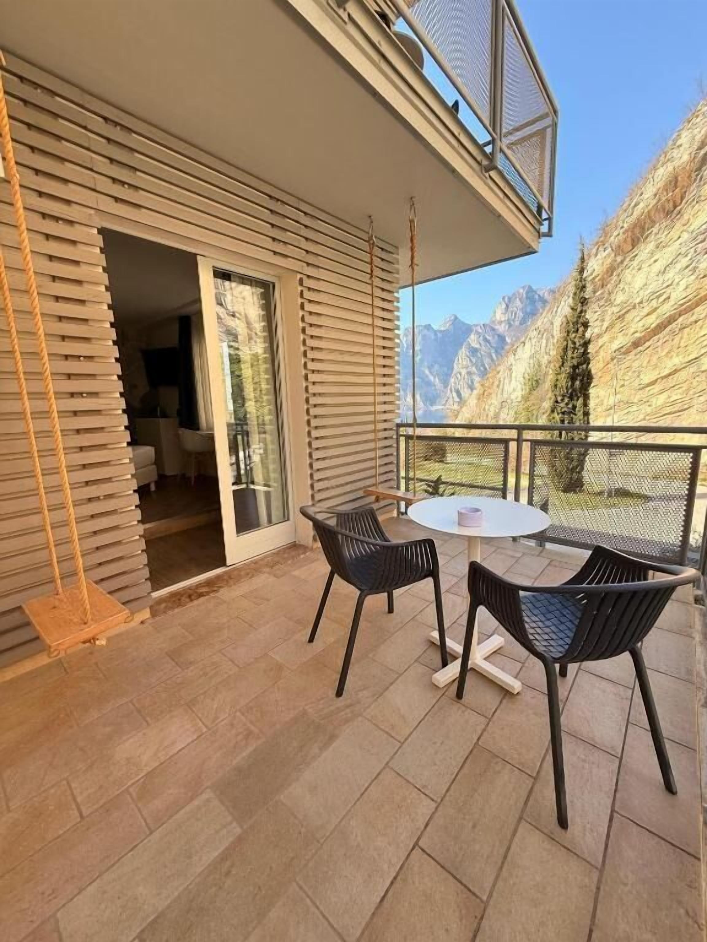 Un balcón con mesa y sillas, una hamaca y vistas a las montañas.