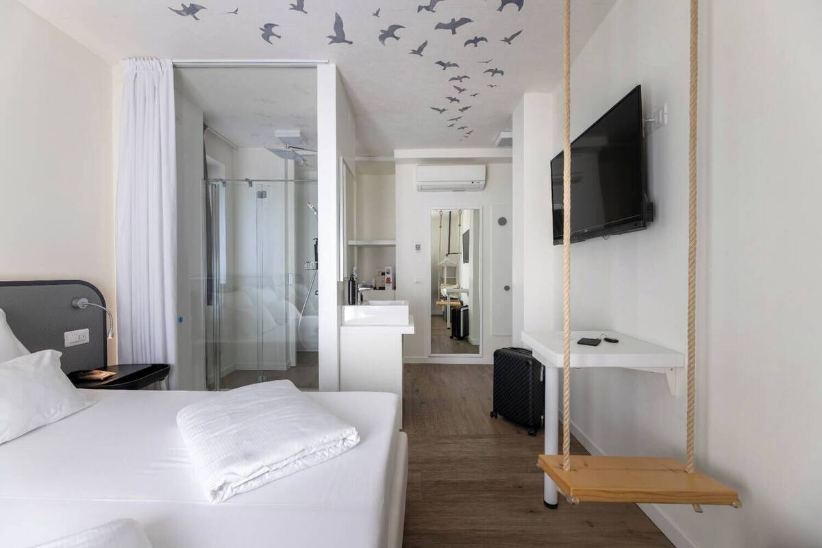 A hotel room with a bed, a TV mounted on the wall, a small desk, and a mirror.