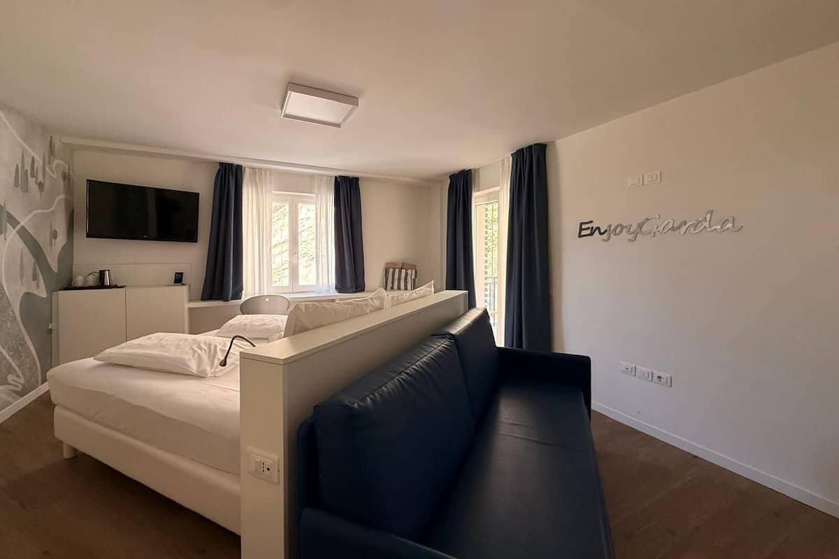 A modern hotel room with a bed, a sofa, a TV, and a wall with the name 'EnvyGandia'.
