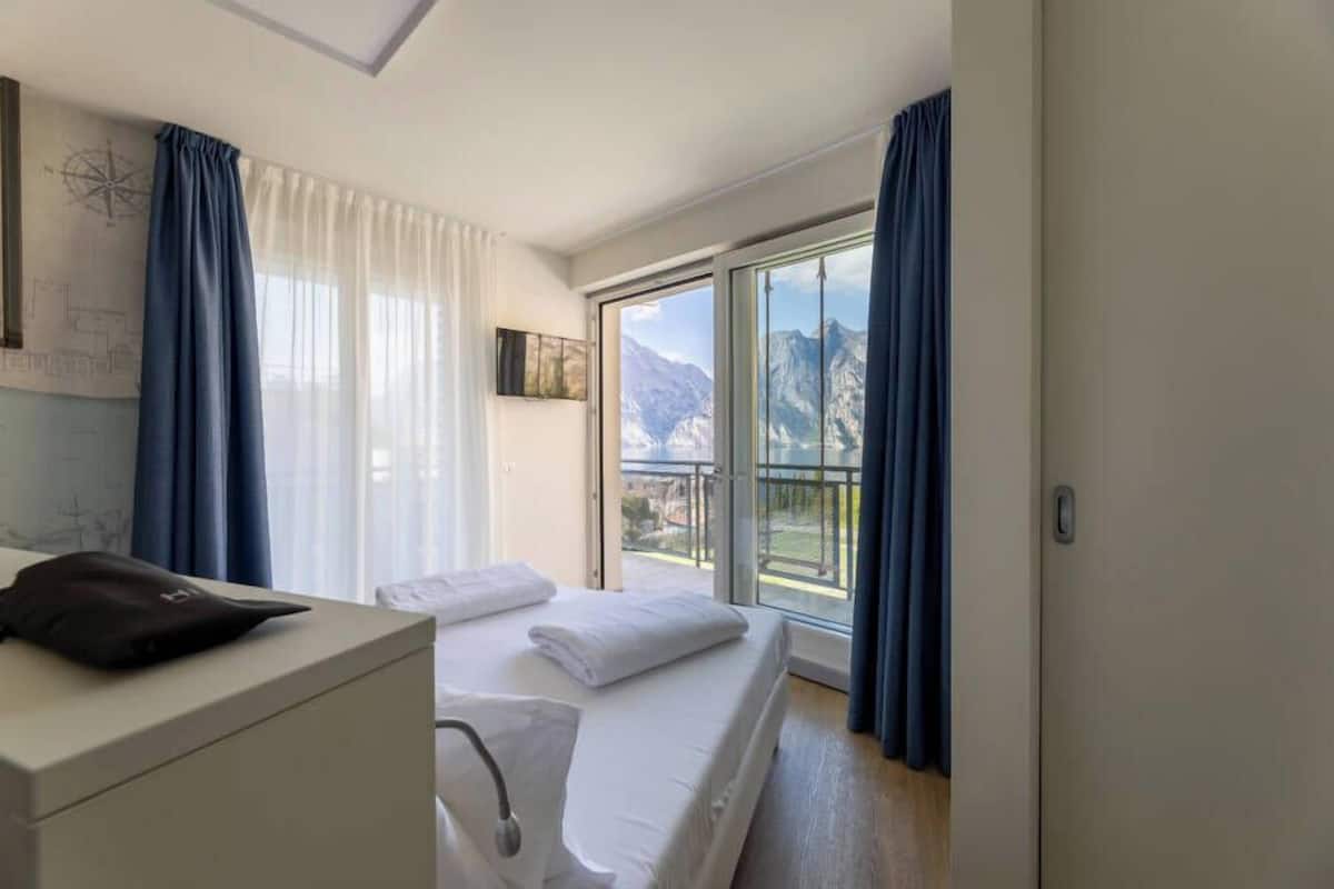 A hotel room with a bed, a desk, and a view of mountains through a large window.