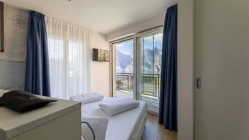 A hotel room with a bed, a desk, and a view of mountains through a large window.