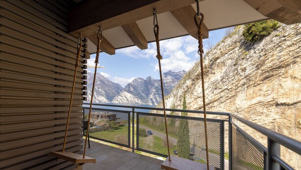 Un balcon avec vue sur les montagnes, une balançoire en bois et une rambarde en métal.