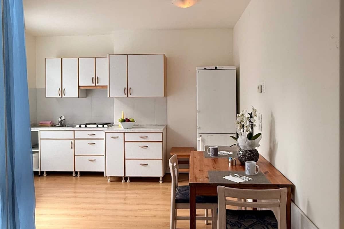 A compact kitchen with white cabinets, a dining table with chairs, and a refrigerator.