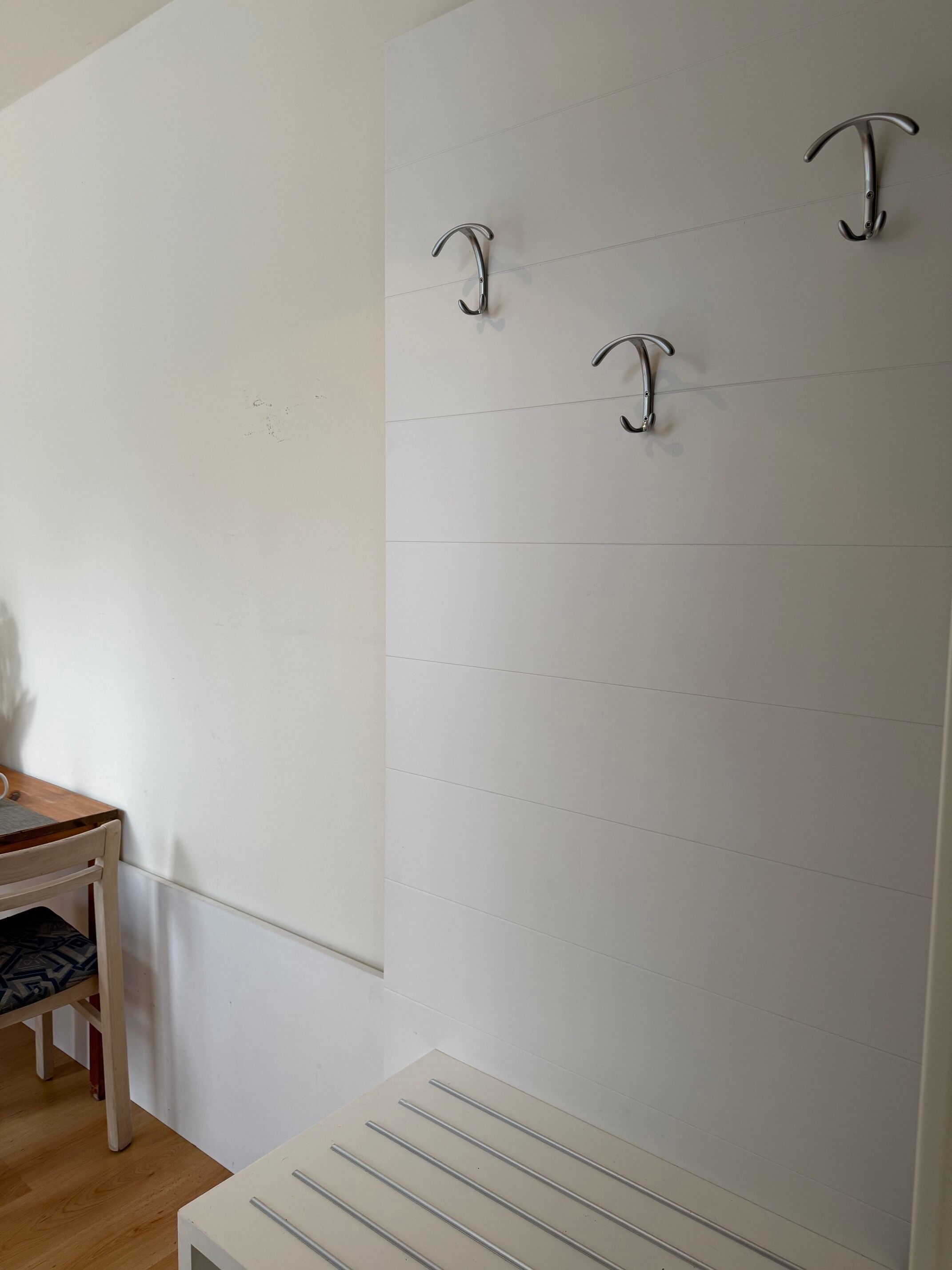 A room with a white wall, a wooden table with a chair, and a radiator.