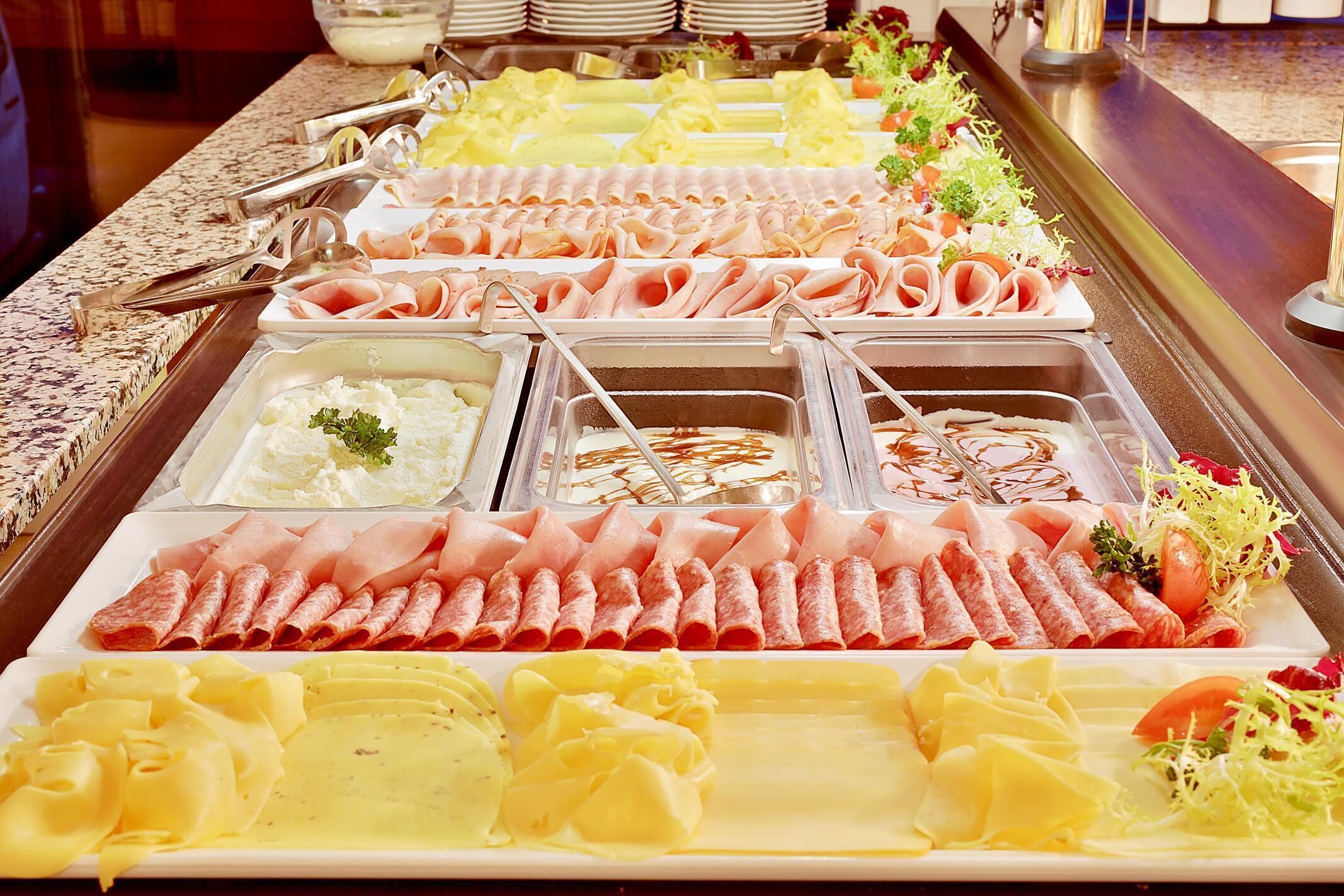 A buffet with various meats, cheeses, and salads.