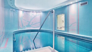 A modern indoor swimming pool with a curved design, surrounded by blue-tiled walls and a ceiling with recessed lighting.