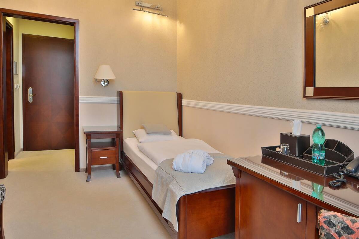 A hotel room with a bed, bedside table, lamp, and a desk with a telephone and toiletries.