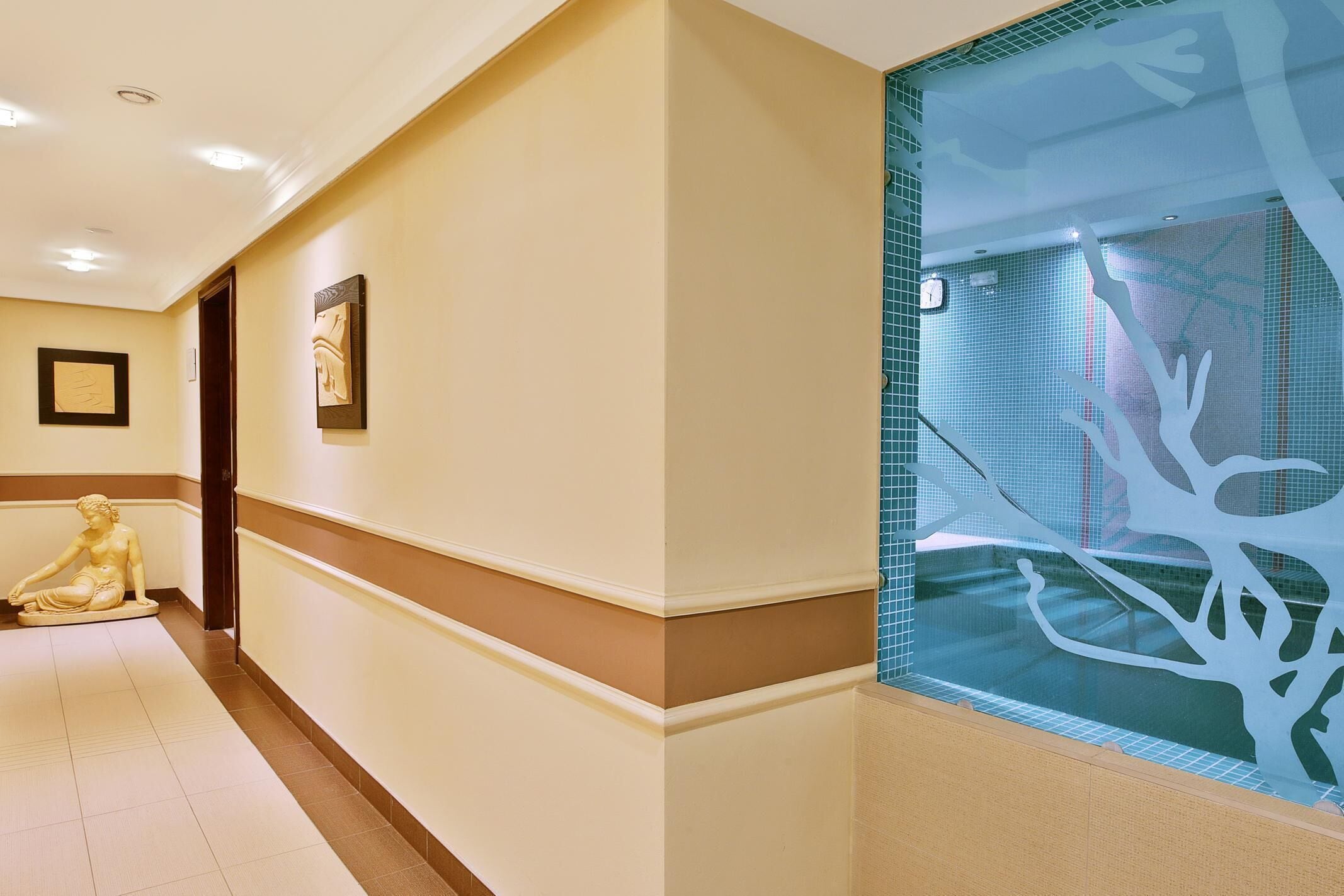 A hotel corridor with a statue, framed artwork, and a decorative glass partition.