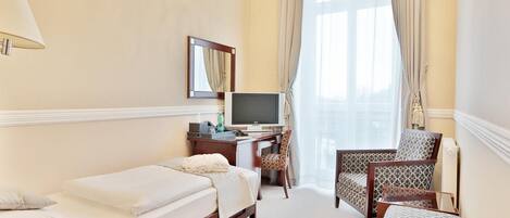 Una habitación de hotel con una cama individual, un escritorio con televisor y dos sillas.