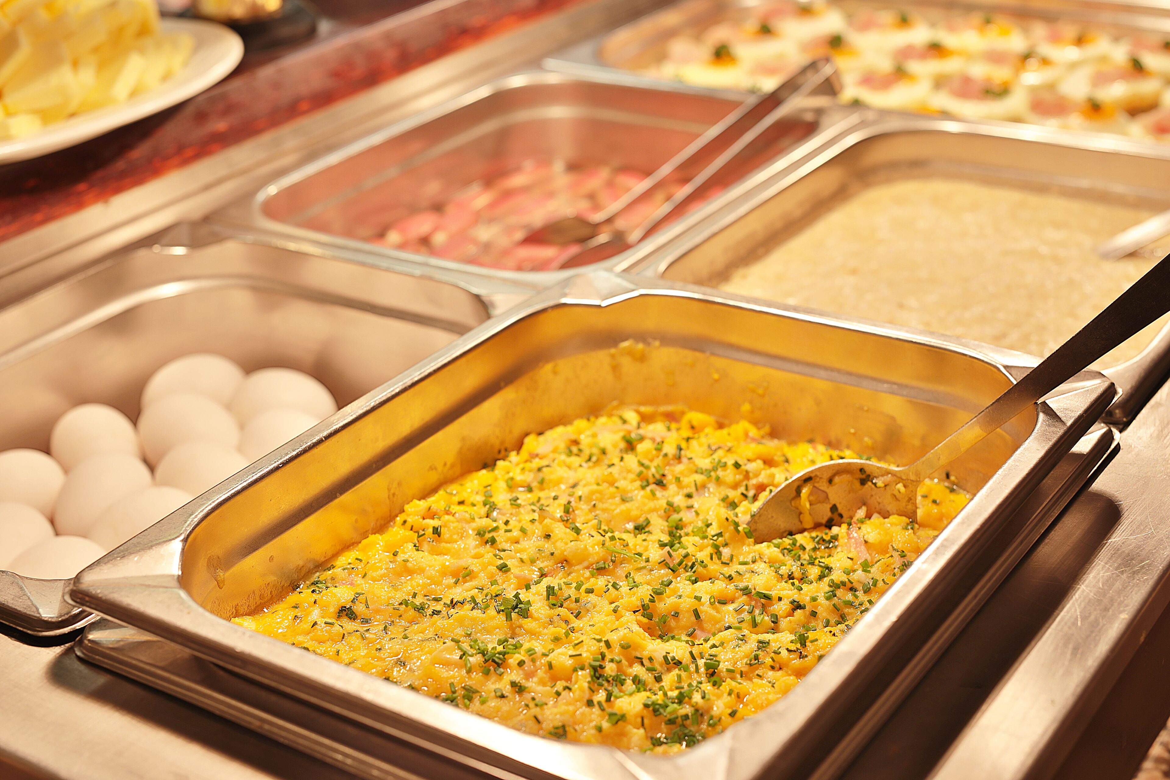 Un bufé con diversas opciones de comida, incluyendo huevos, un plato de cazuela y otras comidas preparadas.