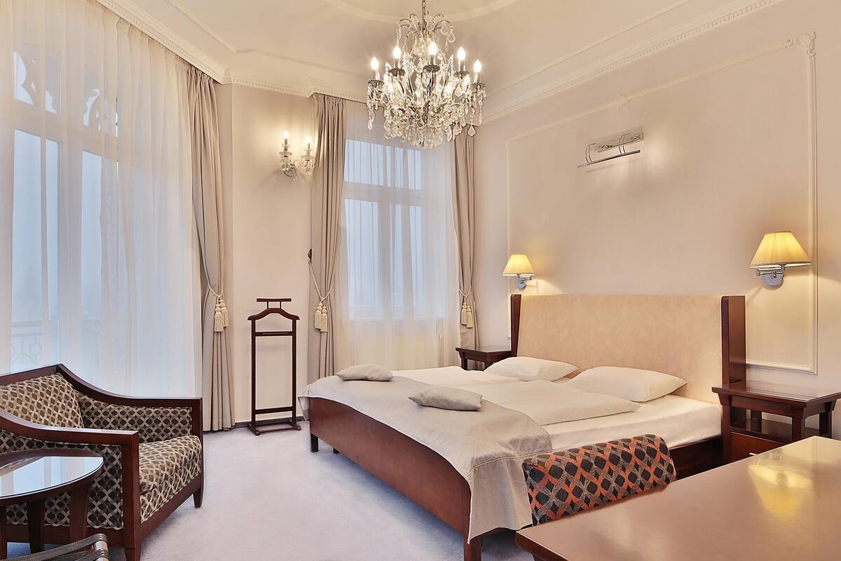 A hotel room with a large bed, a chandelier, a desk, and a chair.
