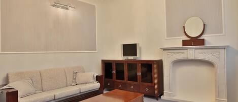 A living room with a sofa, a wooden cabinet, a television, a fireplace, and a chandelier.