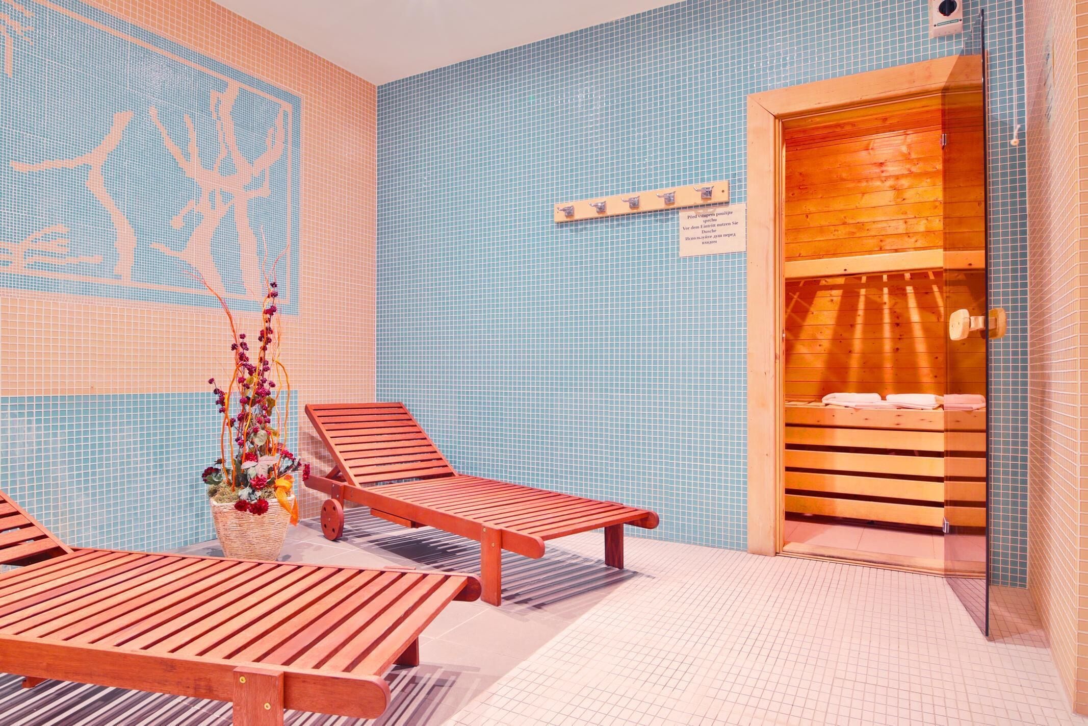 A room with a wooden bench, a wall-mounted shelf with towels, and a wooden door leading to a sauna.