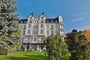 A large, multi-story building with a symmetrical facade, multiple balconies, and a central entrance with steps.