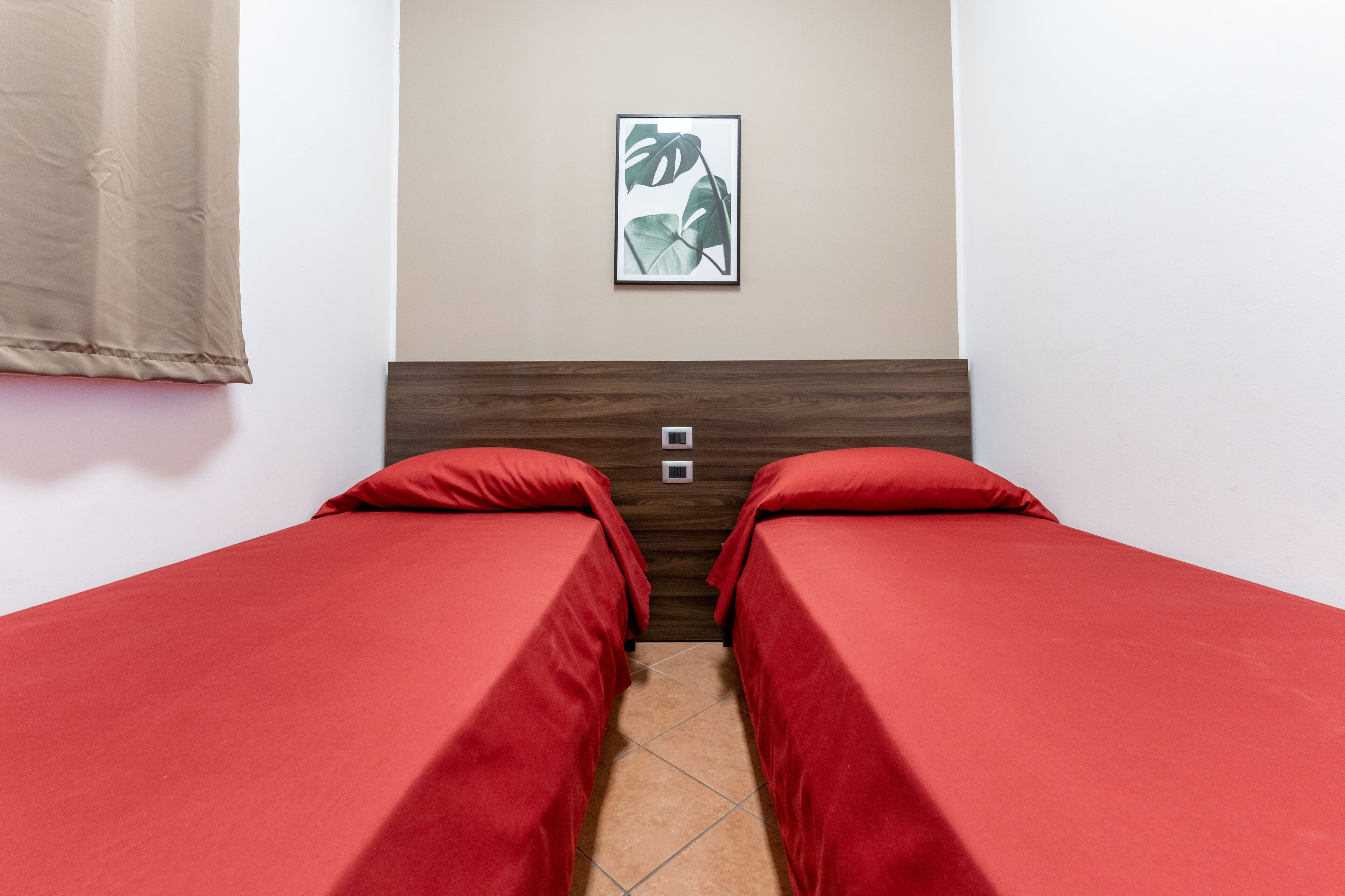 A room with two single beds, a wooden headboard, a framed picture on the wall, and a curtain on the left.