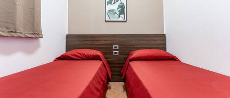 A room with two single beds, a wooden headboard, a framed picture on the wall, and a curtain on the left.