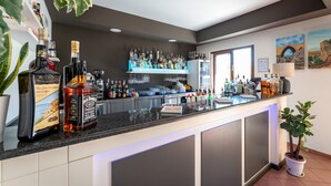 A bar area with a countertop displaying various bottles and glasses, a potted plant, and a window providing natural light. - La Terra dei Sogni Country Hotel (Fiumefreddo di Sicilia)