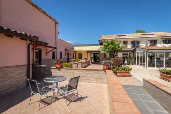 Un patio con mobiliario exterior, plantas en macetas y un edificio de techo de tejas.