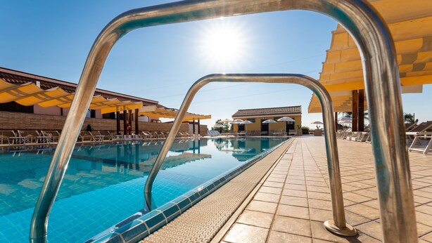 A swimming pool with clear blue water, surrounded by sun umbrellas and lounge chairs. - La Terra dei Sogni Country Hotel (Fiumefreddo di Sicilia)