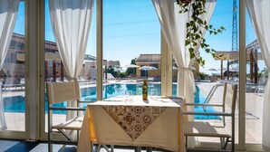 A dining area with a table set for two, overlooking a pool with lounge chairs and umbrellas. - La Terra dei Sogni Country Hotel (Fiumefreddo di Sicilia)