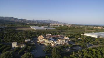 An aerial view of a property with multiple buildings, including a large greenhouse, surrounded by lush greenery and mountains in the background.