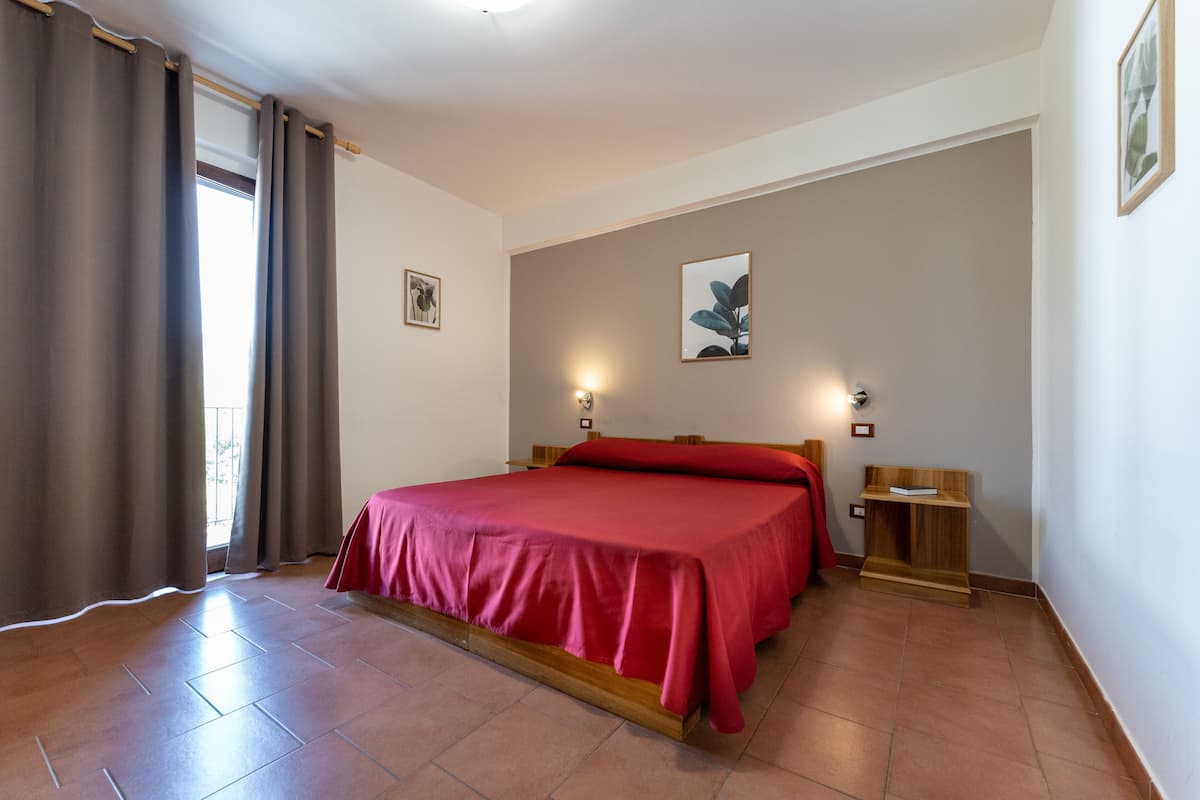 A bedroom with a bed, curtains, a bedside table, and wall-mounted lights.