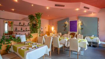 Ein Restaurant mit weißen Tischen und Stühlen, einer großen Pflanze und einer Speisekarte.