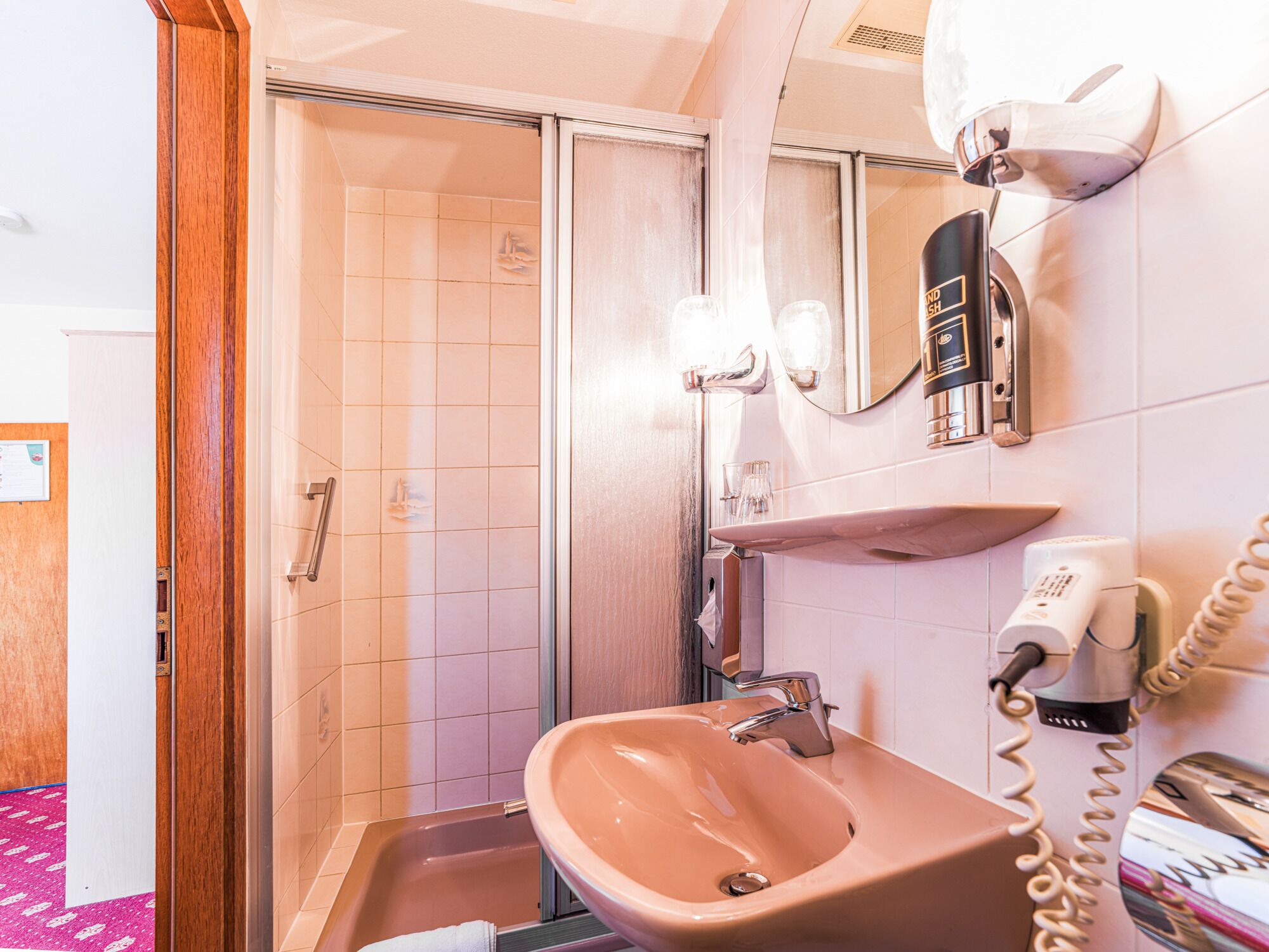 A bathroom with a sink, mirror, hairdryer, and shower.