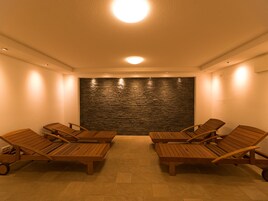 A spa room with a stone wall, wooden lounge chairs, and a ceiling light.