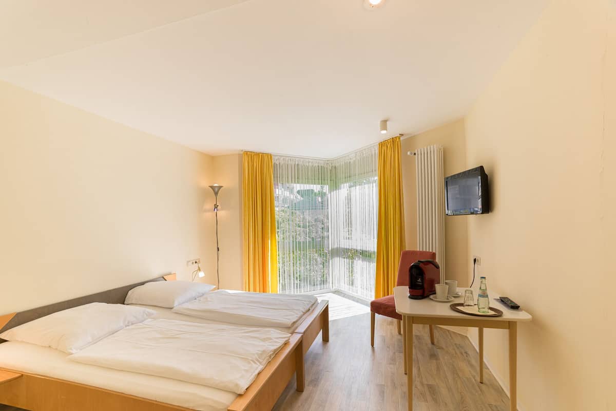 Een hotelkamer met een bed, een bureau met stoel, een televisie en een raam met gordijnen.