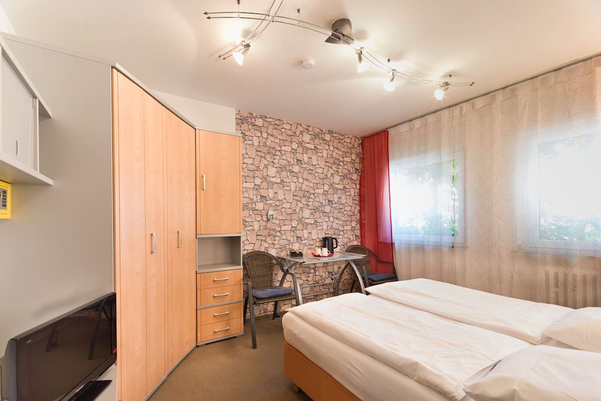Een hotelkamer met een bed, een televisie, een bureau met stoel, een kledingkast en een stenen muur.